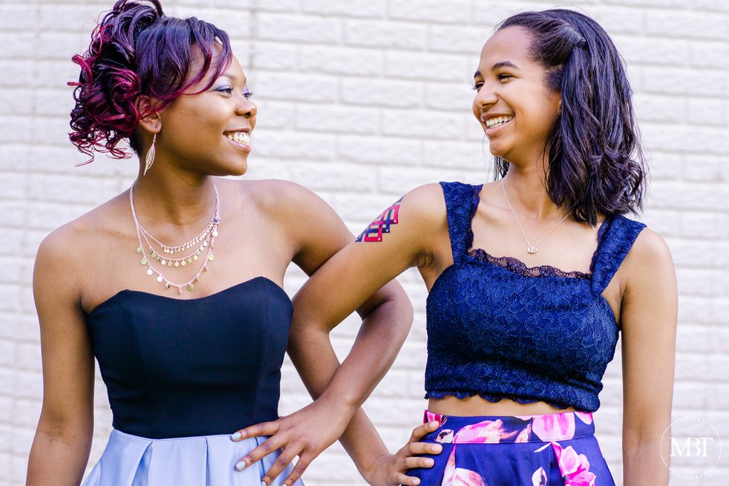 best friends smiling & looking at each other with their arms linked, taken on their prom night at a backyard in Fairfax, Virginia taken by a Northern Virginia portrait photographer