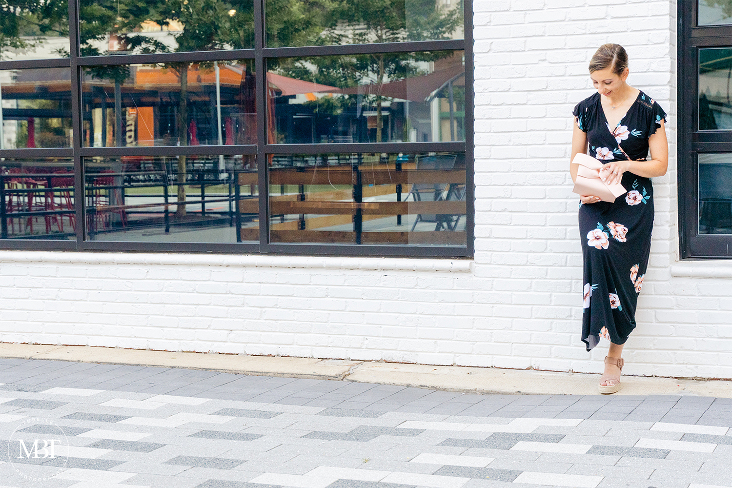 woman wearing black floral maxi dress looking at her beige clutch by a white wall, fashion session taken in Arlington, Virginia by a lifestyle photographer in Washington, DC