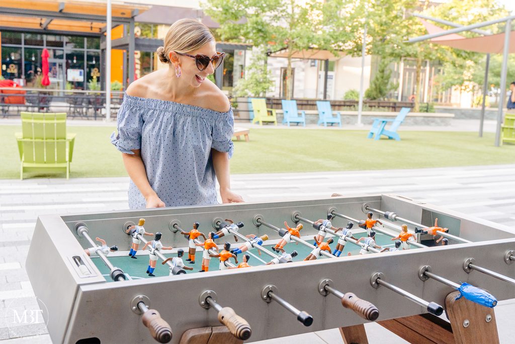 woman wearing blue striped off the shoulder top playing in the foosball table, lifestyle session taken in Arlington, Virginia by a personal branding photographer in Virginia